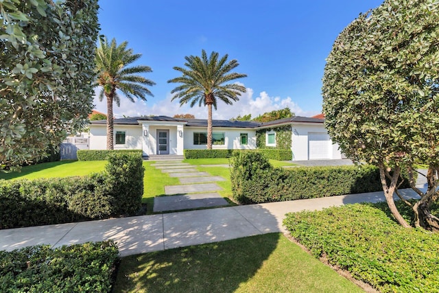 ranch-style home featuring roof mounted solar panels, stucco siding, an attached garage, and a front lawn