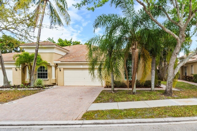 mediterranean / spanish-style home featuring stucco siding, a tile roof, decorative driveway, and a garage