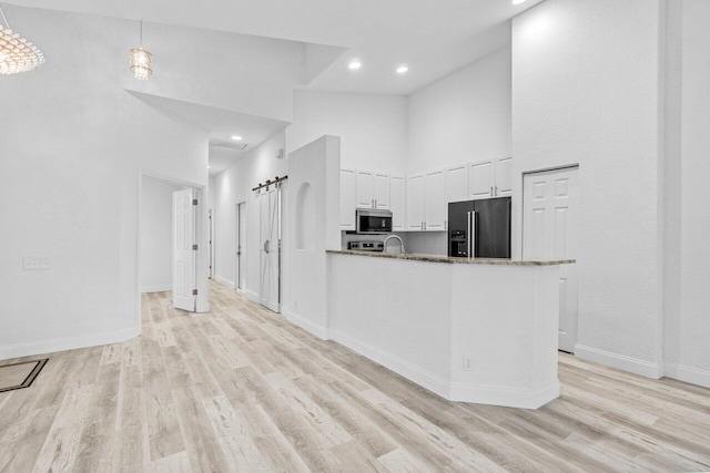 kitchen featuring light wood-style flooring, a high ceiling, white cabinets, stainless steel microwave, and high end black fridge