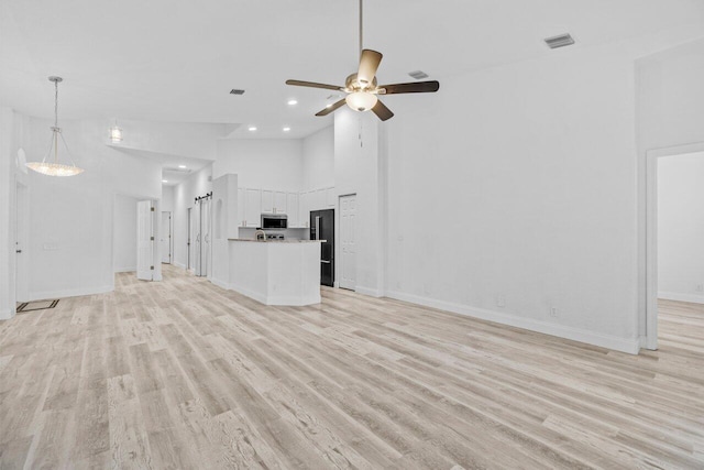 unfurnished living room featuring light wood-style flooring, a ceiling fan, visible vents, and high vaulted ceiling