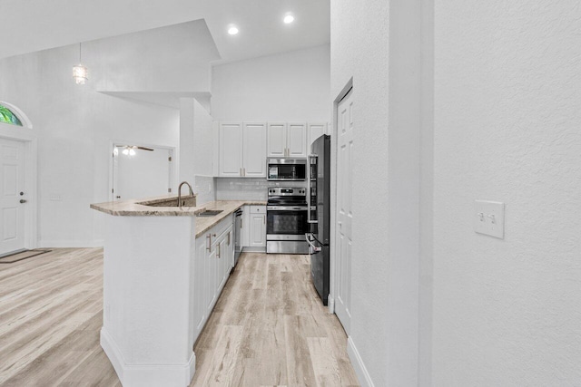 kitchen featuring white cabinetry, a peninsula, a high ceiling, and stainless steel appliances