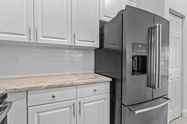 kitchen with white cabinetry, light stone counters, stainless steel refrigerator with ice dispenser, and backsplash