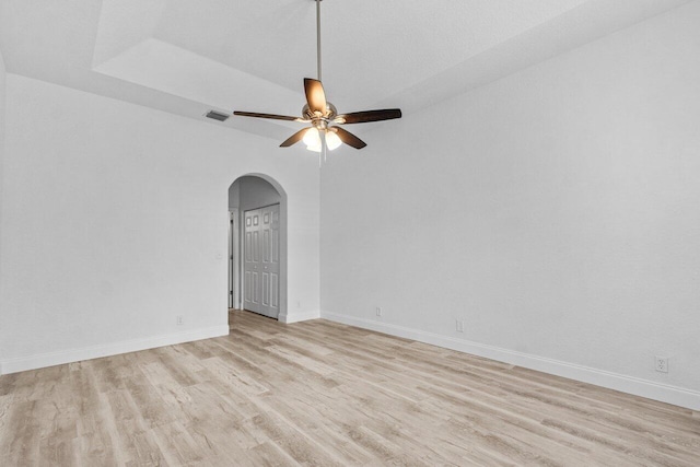 spare room featuring light wood-type flooring, visible vents, arched walkways, and baseboards