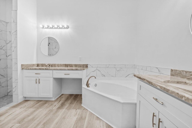 full bathroom with a bath, two vanities, wood finished floors, and a sink