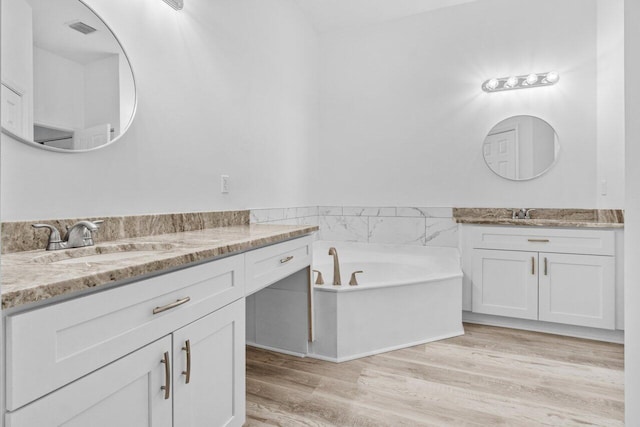 full bathroom featuring visible vents, two vanities, a sink, wood finished floors, and a bath