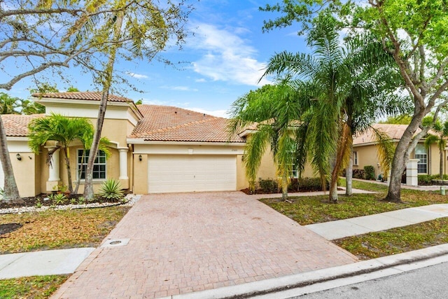 mediterranean / spanish home featuring stucco siding, a tile roof, decorative driveway, and a garage