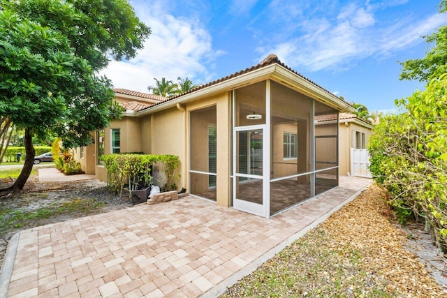 rear view of house featuring a patio, a tile roof, a sunroom, and stucco siding