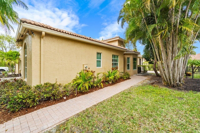 view of side of property with stucco siding, a tile roof, a lawn, and fence