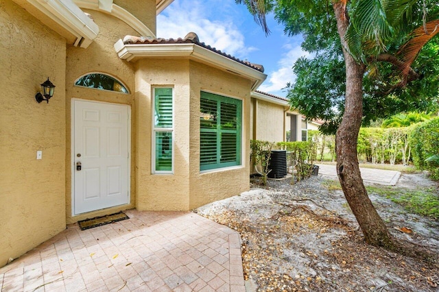 doorway to property featuring central air condition unit, stucco siding, and a tiled roof