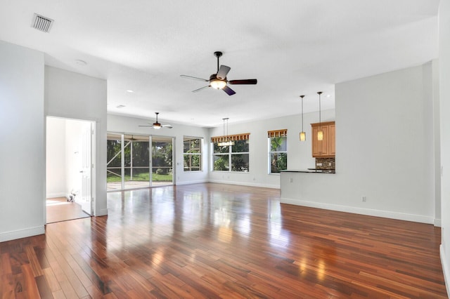 unfurnished living room with hardwood / wood-style floors, baseboards, visible vents, and a ceiling fan