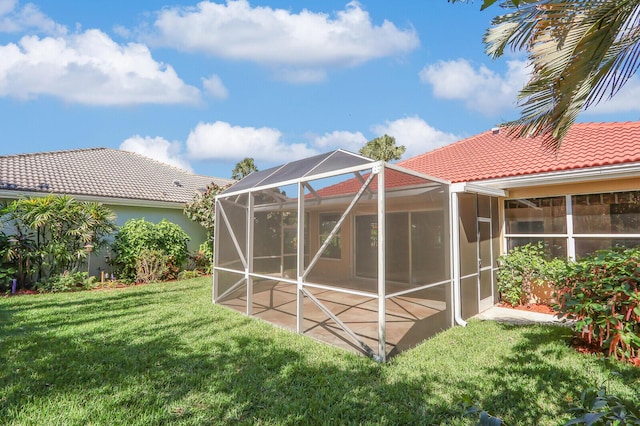 rear view of property with glass enclosure, a tile roof, and a yard