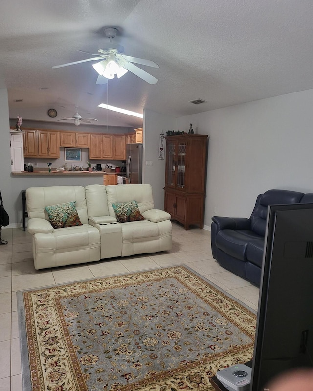 living room with light tile patterned floors, visible vents, a textured ceiling, and baseboards