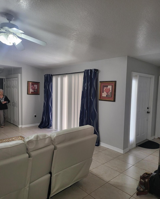 living area with light tile patterned flooring, baseboards, a textured ceiling, and a ceiling fan