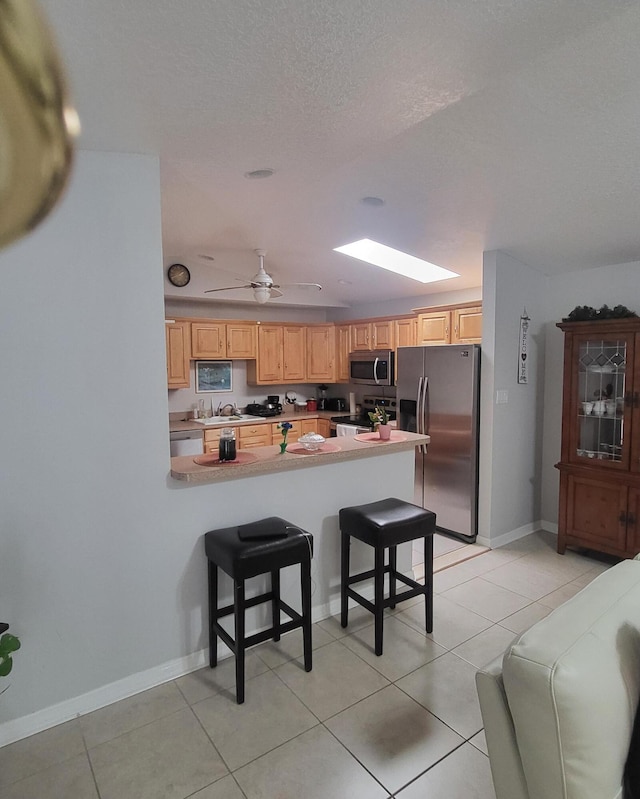 kitchen featuring a breakfast bar area, appliances with stainless steel finishes, a peninsula, light tile patterned flooring, and a sink