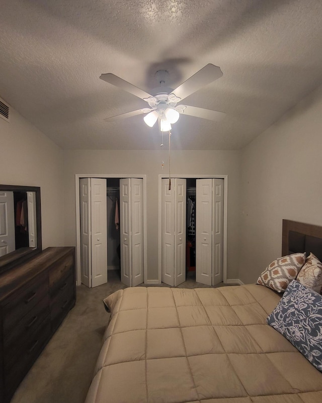 bedroom with visible vents, two closets, carpet, a textured ceiling, and a ceiling fan