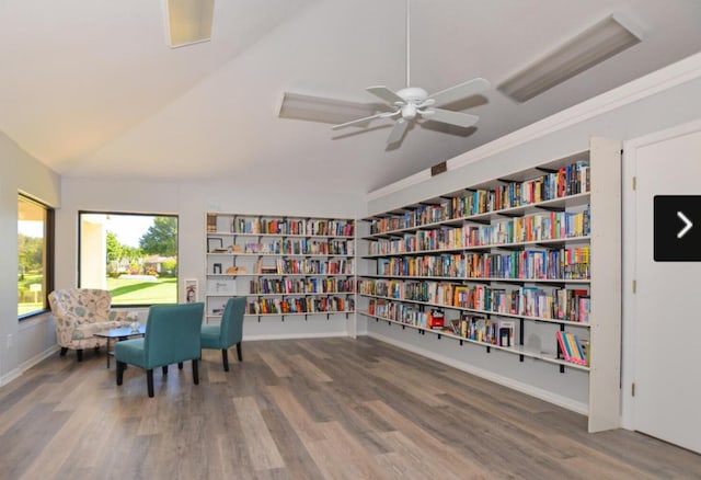 sitting room with built in shelves, a ceiling fan, wood finished floors, vaulted ceiling, and bookshelves