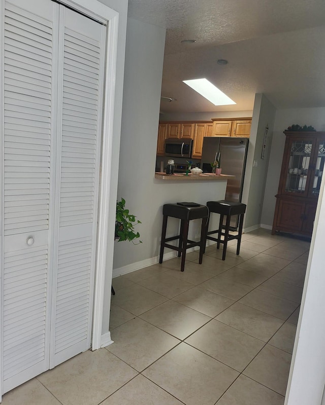 kitchen with a kitchen breakfast bar, stainless steel appliances, a skylight, light tile patterned flooring, and baseboards