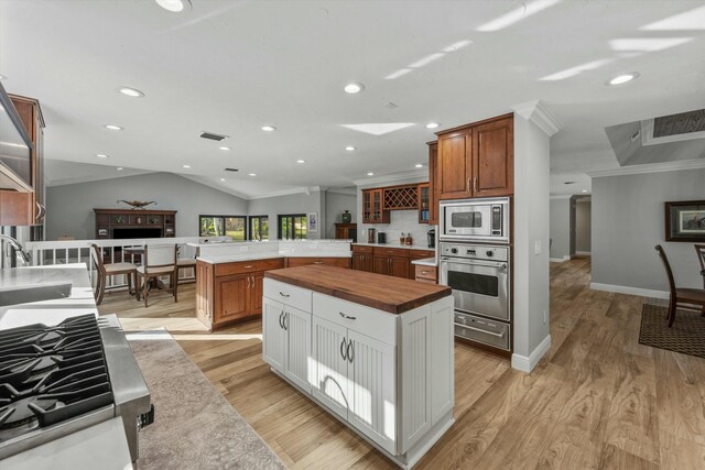 kitchen with glass insert cabinets, butcher block countertops, ornamental molding, light wood-style floors, and stainless steel appliances