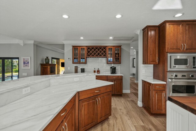 kitchen with ornamental molding, glass insert cabinets, appliances with stainless steel finishes, light wood-type flooring, and backsplash