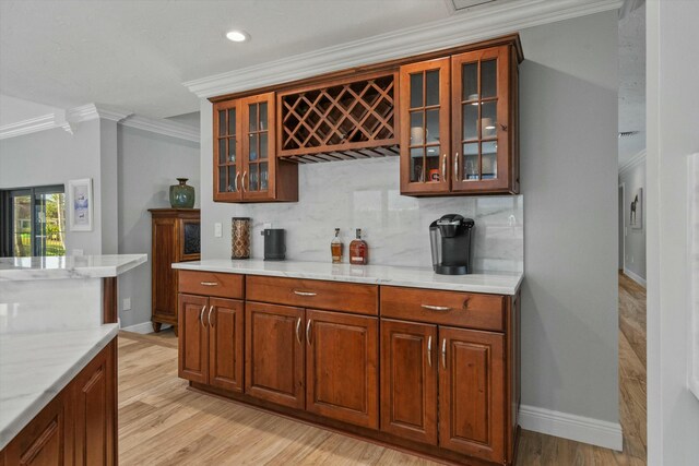 bar with light wood-style flooring, backsplash, crown molding, baseboards, and a dry bar