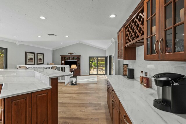 kitchen featuring light stone counters, visible vents, vaulted ceiling, glass insert cabinets, and light wood-type flooring