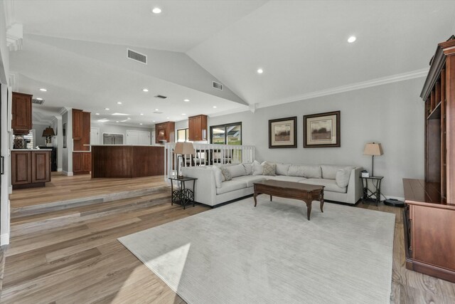 living area featuring visible vents, crown molding, light wood-type flooring, and lofted ceiling