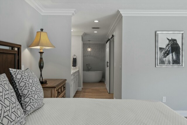 bedroom with visible vents, crown molding, a barn door, and wood finished floors