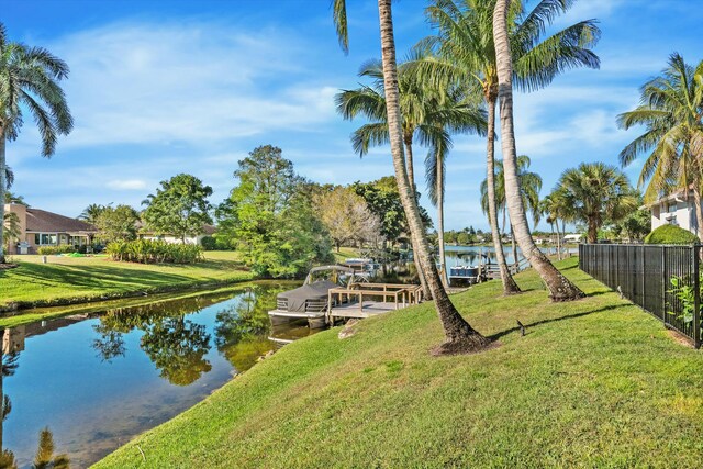 view of dock with a water view, a lawn, and fence