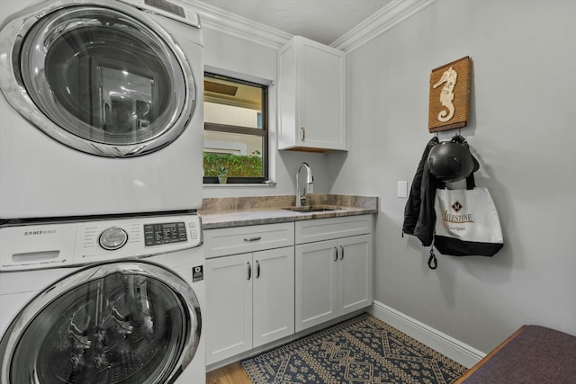 laundry area featuring baseboards, cabinet space, ornamental molding, a sink, and stacked washer / drying machine