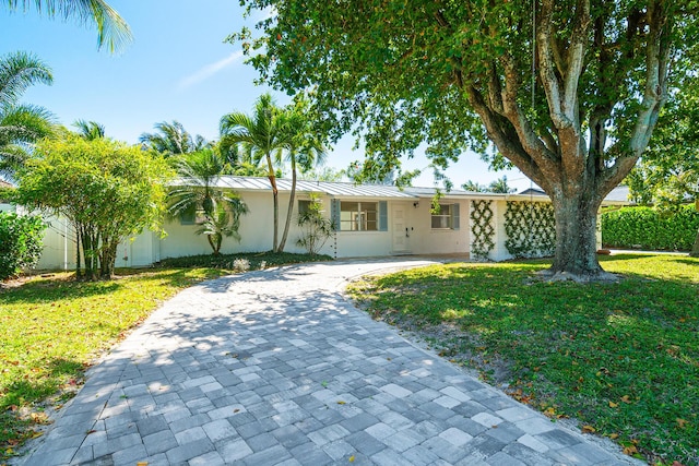 ranch-style house featuring stucco siding, metal roof, decorative driveway, and a front lawn