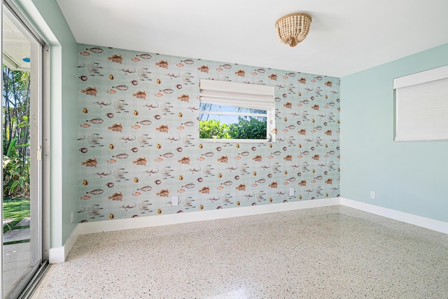 unfurnished room with wallpapered walls, speckled floor, and baseboards