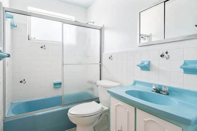 bathroom featuring vanity, a wainscoted wall, tile walls, toilet, and combined bath / shower with glass door