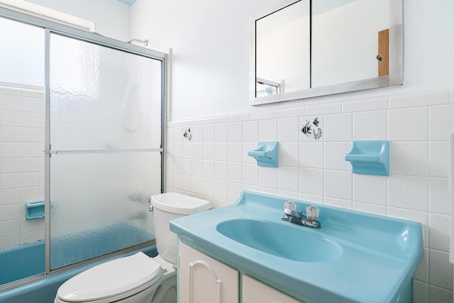 bathroom with enclosed tub / shower combo, toilet, tile walls, and vanity