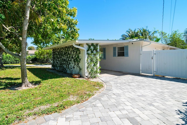 view of front of home with an attached carport, a front lawn, stucco siding, decorative driveway, and a gate