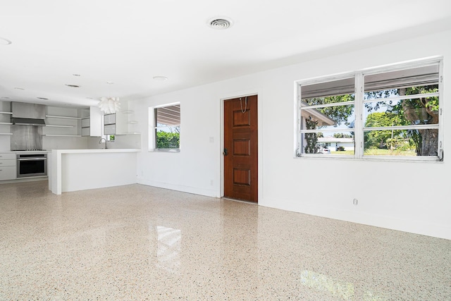 unfurnished living room with visible vents, speckled floor, baseboards, and a sink