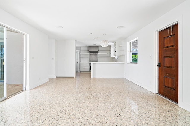 unfurnished living room with baseboards, light speckled floor, and an inviting chandelier