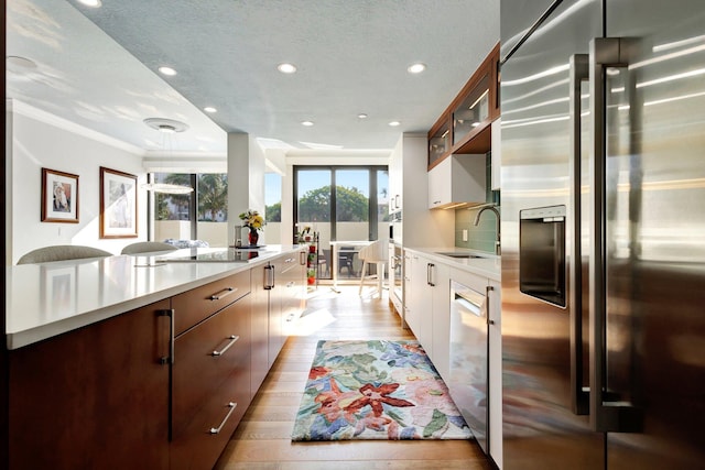 kitchen with light countertops, black electric cooktop, stainless steel refrigerator with ice dispenser, and a sink