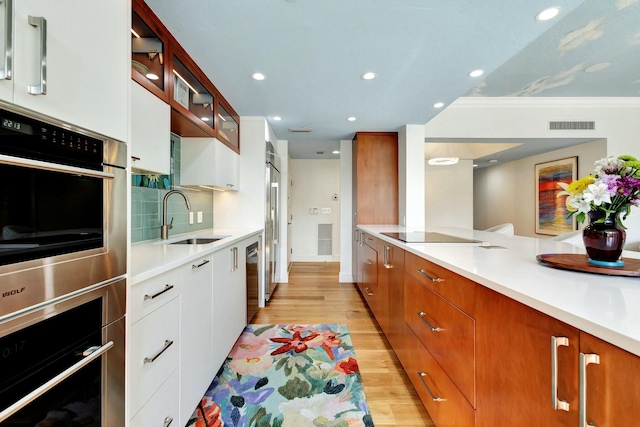 kitchen with tasteful backsplash, glass insert cabinets, light countertops, light wood-style flooring, and a sink