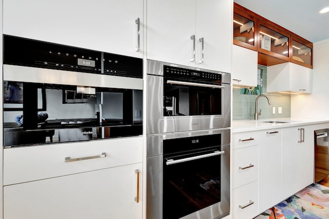 kitchen with decorative backsplash, white cabinetry, stainless steel double oven, and a sink