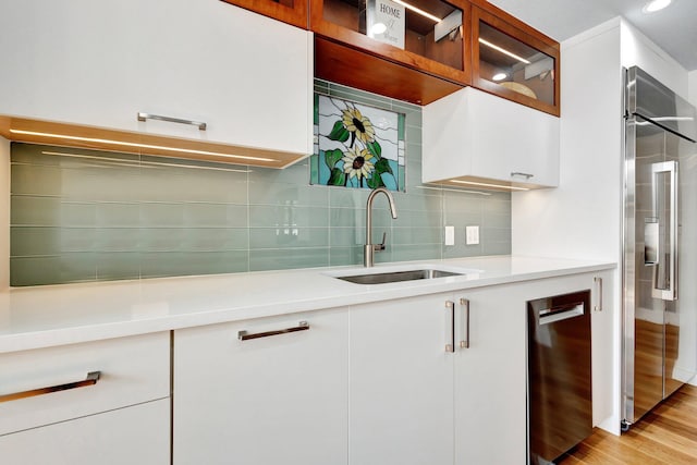 kitchen with tasteful backsplash, light countertops, high quality fridge, white cabinets, and a sink