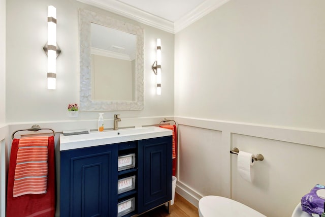 bathroom with vanity, wood finished floors, a wainscoted wall, ornamental molding, and toilet