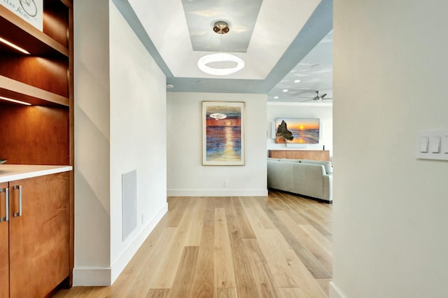 corridor featuring baseboards, a raised ceiling, and light wood-style floors