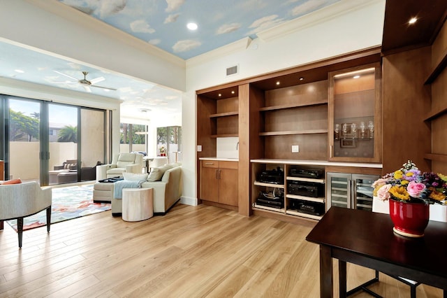 living area featuring light wood finished floors, visible vents, a ceiling fan, and ornamental molding