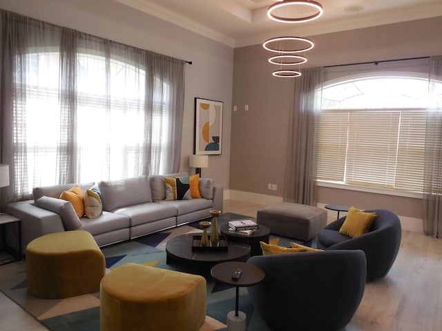 living area with a tray ceiling, wood finished floors, baseboards, and ornamental molding