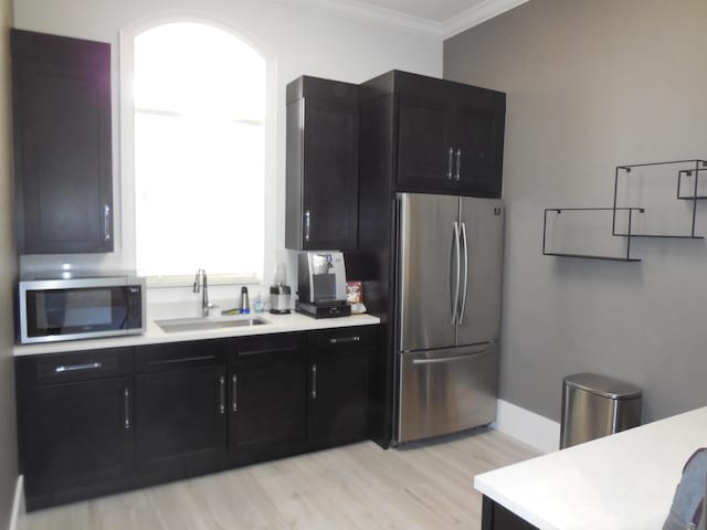 kitchen featuring a sink, crown molding, light countertops, stainless steel appliances, and dark cabinets