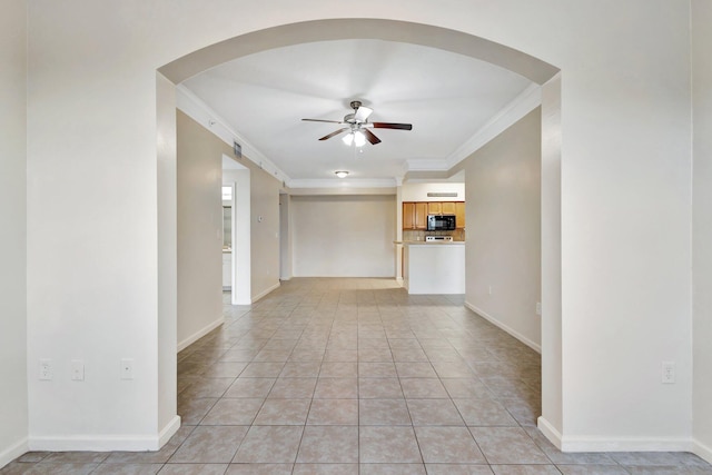 empty room with baseboards, ornamental molding, light tile patterned floors, arched walkways, and a ceiling fan