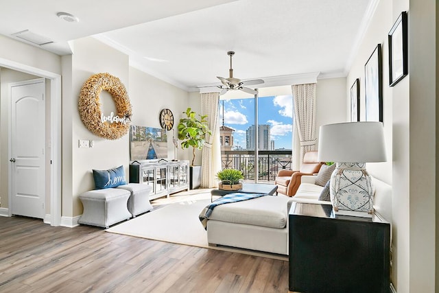 living room with ceiling fan, wood finished floors, baseboards, and ornamental molding