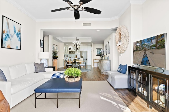 living room with a tray ceiling, visible vents, wood finished floors, and crown molding