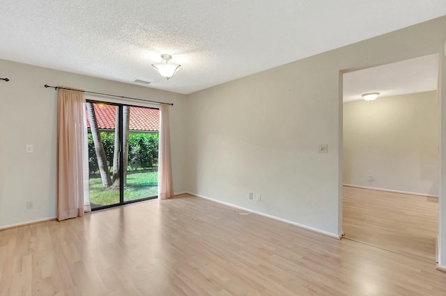 spare room featuring light wood-type flooring, baseboards, a textured ceiling, and visible vents