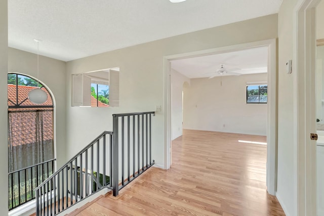 hall with wood finished floors, an upstairs landing, baseboards, and arched walkways
